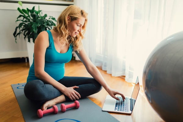 Woman sitting on exercise mat and using laptop at home