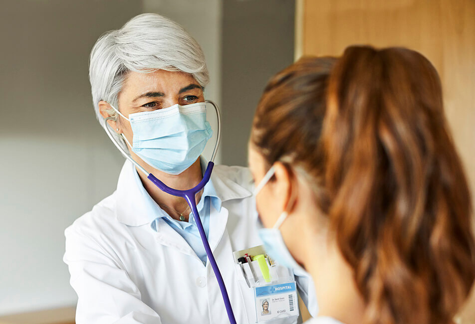 Doctor examining female through stethoscope in ICU