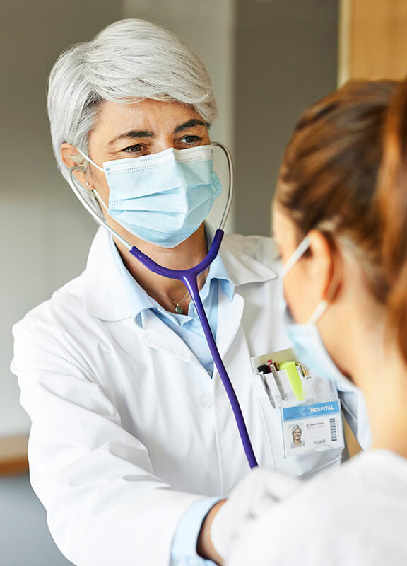 Doctor examining female through stethoscope in ICU